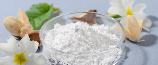 Allantoin Pulver in einer Schüssel umgeben von Blumen und Blättern, ideal für Hautregeneration und Beruhigung.